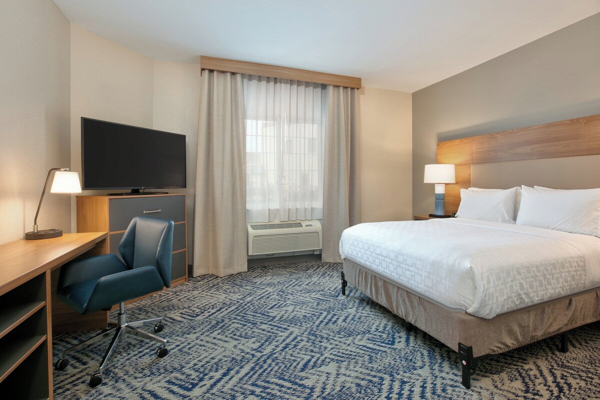 Habitación de hotel con cama, escritorio, silla, televisor y ventana con cortinas.