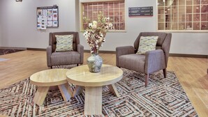 Un vestíbulo con dos sillones, una mesa redonda, un jarrón con flores y un tablón de anuncios con información sobre las habitaciones.