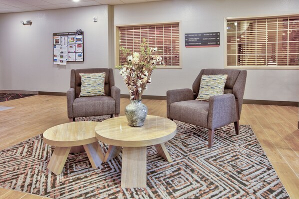 Un vestíbulo con dos sillones, una mesa redonda, un jarrón con flores y un tablón de anuncios con información sobre las habitaciones.