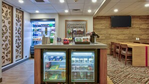 Una estación de bebidas de autoservicio con dos congeladores refrigerados, un letrero que dice Candlewood Cupboard y un televisor de pantalla plana montado en la pared.