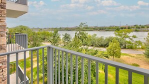 Un balcón con vista a un río, vegetación y edificios a lo lejos.