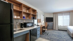Una habitación de hotel compacta con kitchenette, una cama, un escritorio y un televisor.