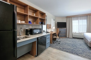 Una habitación de hotel compacta con kitchenette, una cama, un escritorio y un televisor.
