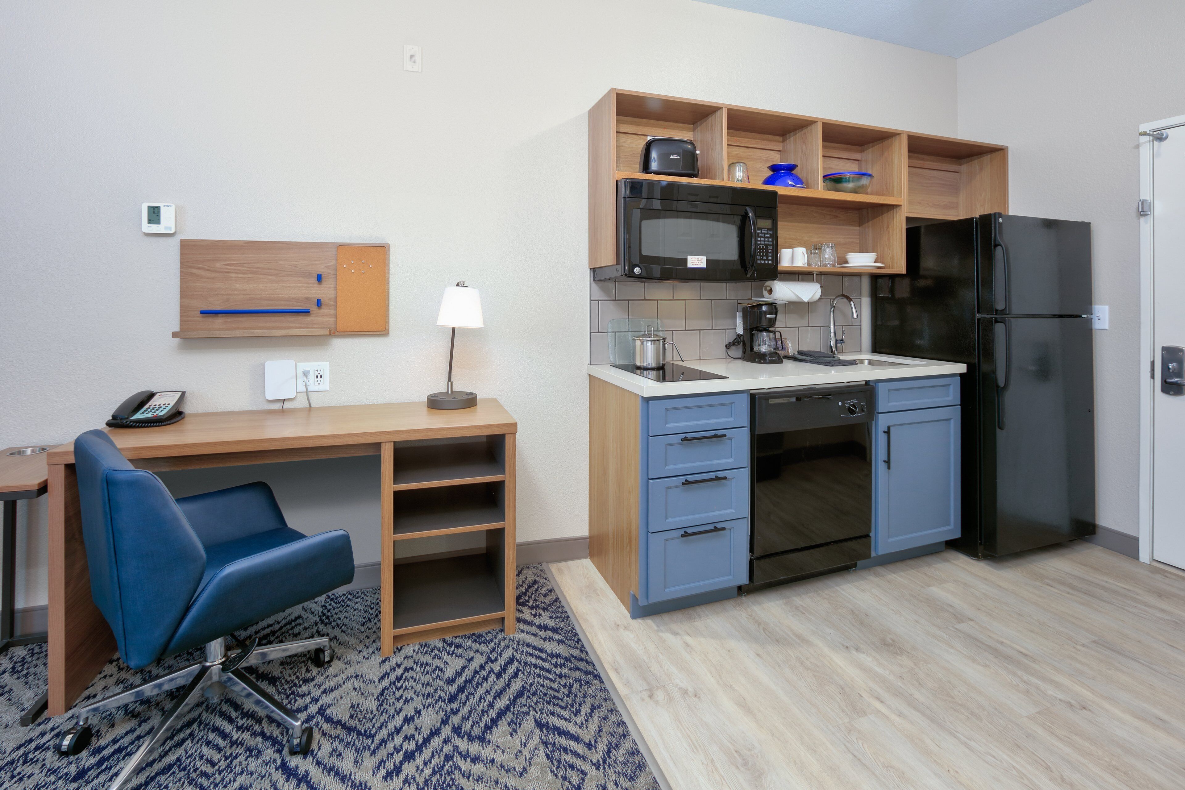Une cuisine compacte équipée d’un four à micro-ondes, d’un réfrigérateur et d’un four encastré. On y trouve également un bureau en bois avec une chaise et un téléphone.