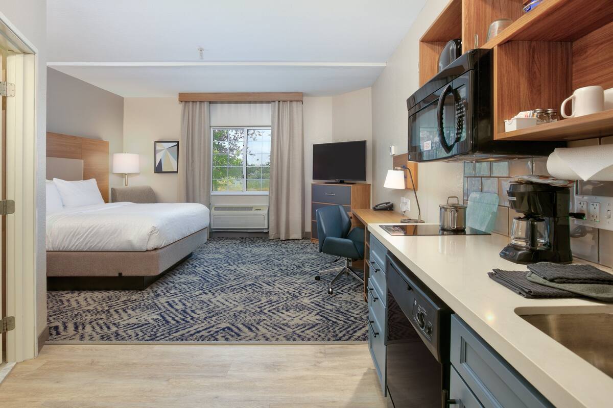 A hotel room with a bed, desk, microwave, and kitchenette.