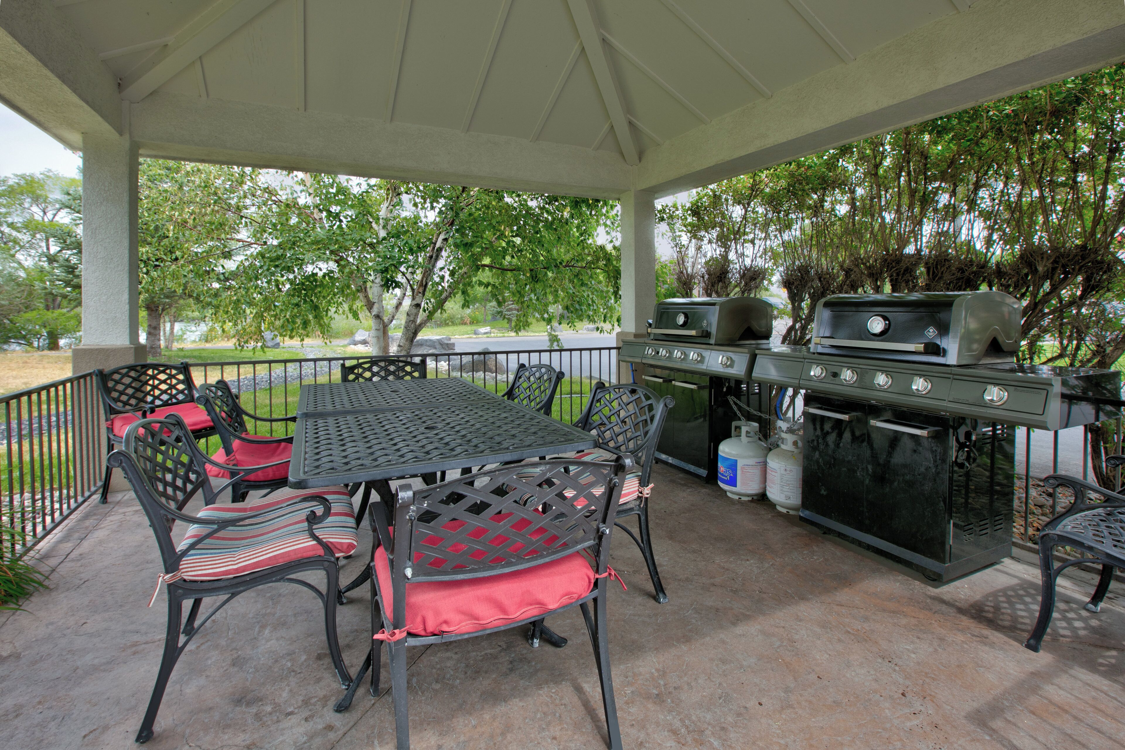 An outdoor patio with a grill, seating, and a view of trees.
