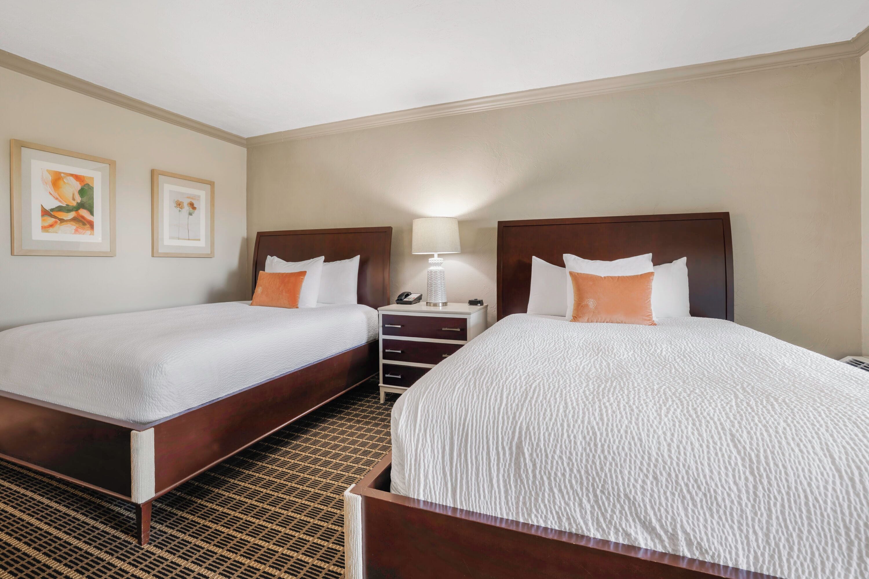 A hotel room with two beds, a nightstand, and a lamp.