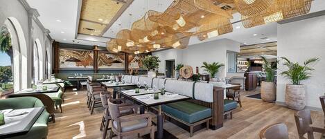 A modern restaurant with wooden flooring, green upholstered seating, and a unique ceiling design.