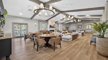 A spacious living room with a fireplace, wooden flooring, and a large dining area with round tables and chairs.