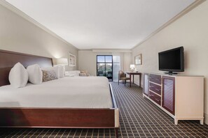 A hotel room with a large bed, a television, a desk, and a view of the outdoors.