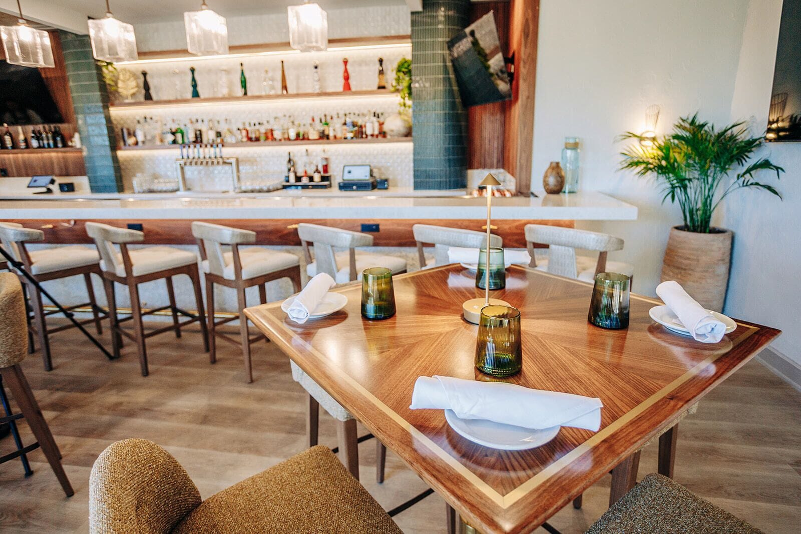 A restaurant with a bar area, wooden tables, and chairs.