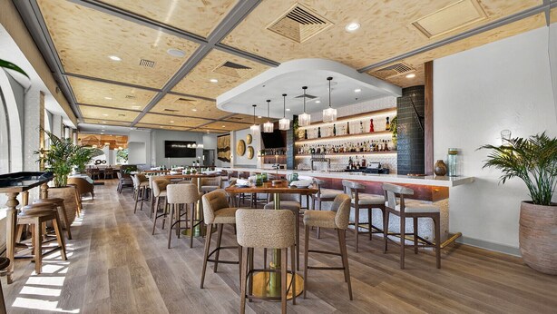 A modern restaurant with wooden flooring, bar seating, and a high ceiling with exposed beams. - Mission Resort and Club (Howey-in-the-Hills)