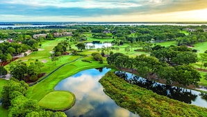 A golf course with a pond, surrounded by lush greenery and trees. - Mission Resort and Club (Howey-in-the-Hills)