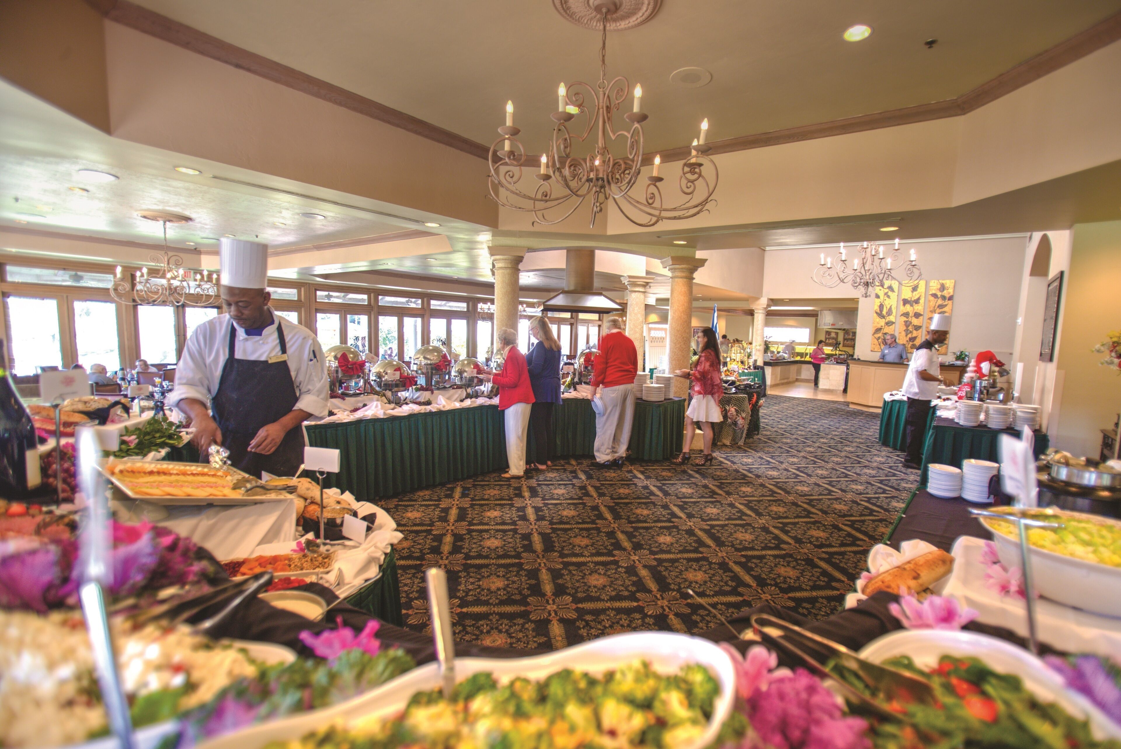 A buffet setup with multiple food stations, a chandelier, and a patterned carpet.