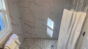 A bathroom with a shower, marble walls, and a geometric tile floor. - The Inn of Dayville (Dayville)