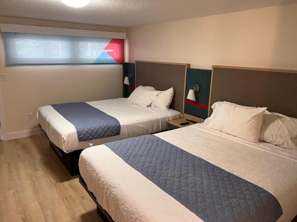 A hotel room with two beds, each with a headboard and bedside lamps.