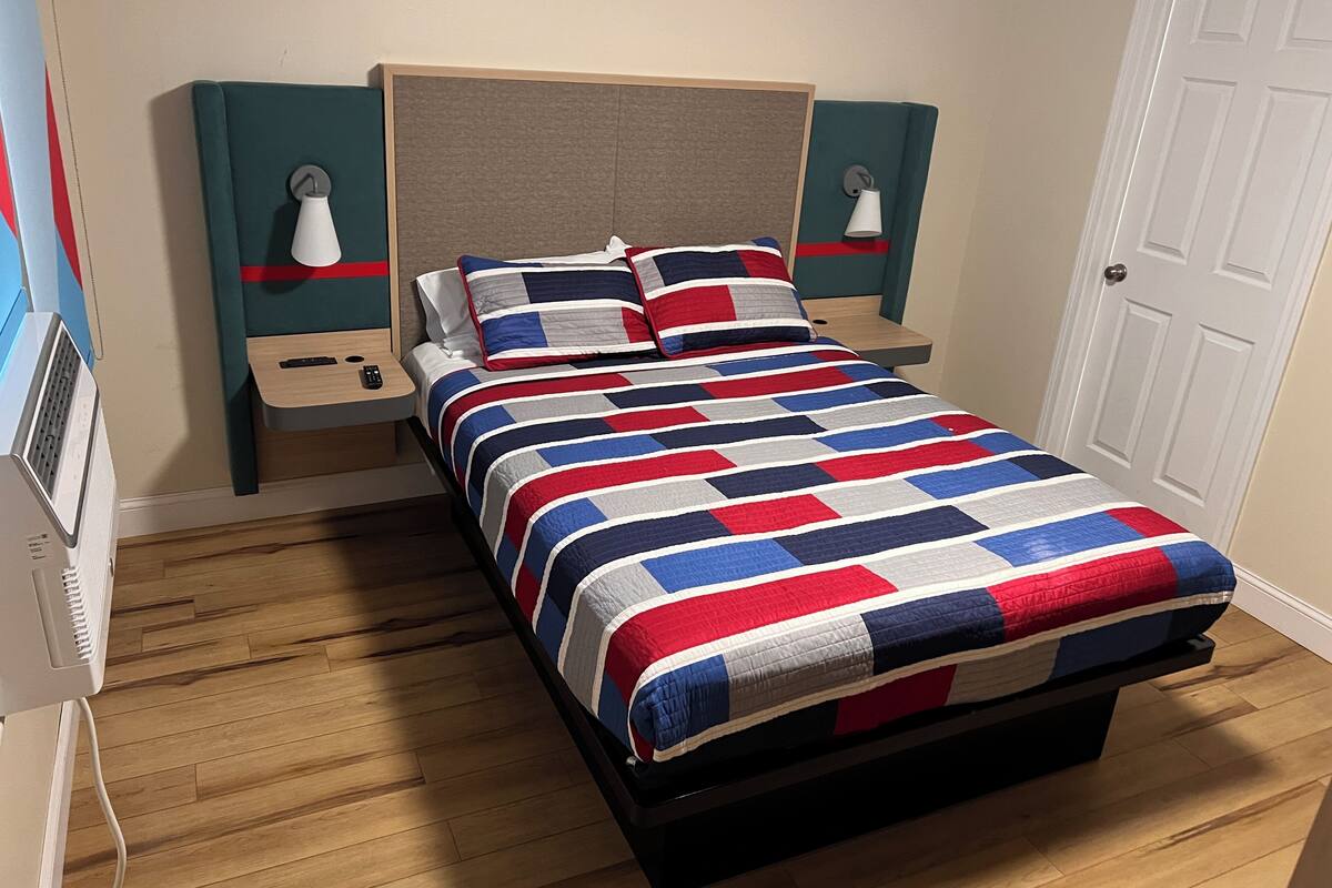 A neatly made bed with a striped bedspread, two bedside tables with lamps, a wooden floor, and a white door.