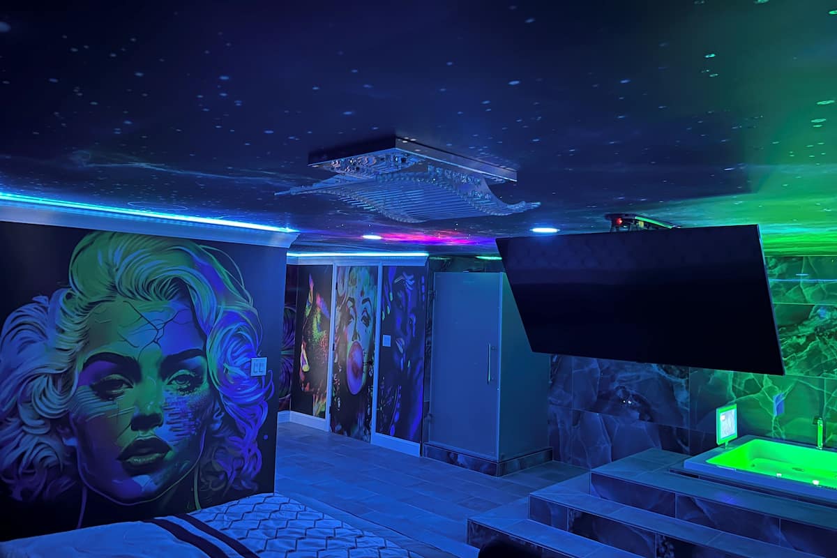 A room with a starry ceiling, a large mural, a flat-screen TV, and a green-lit bathtub.