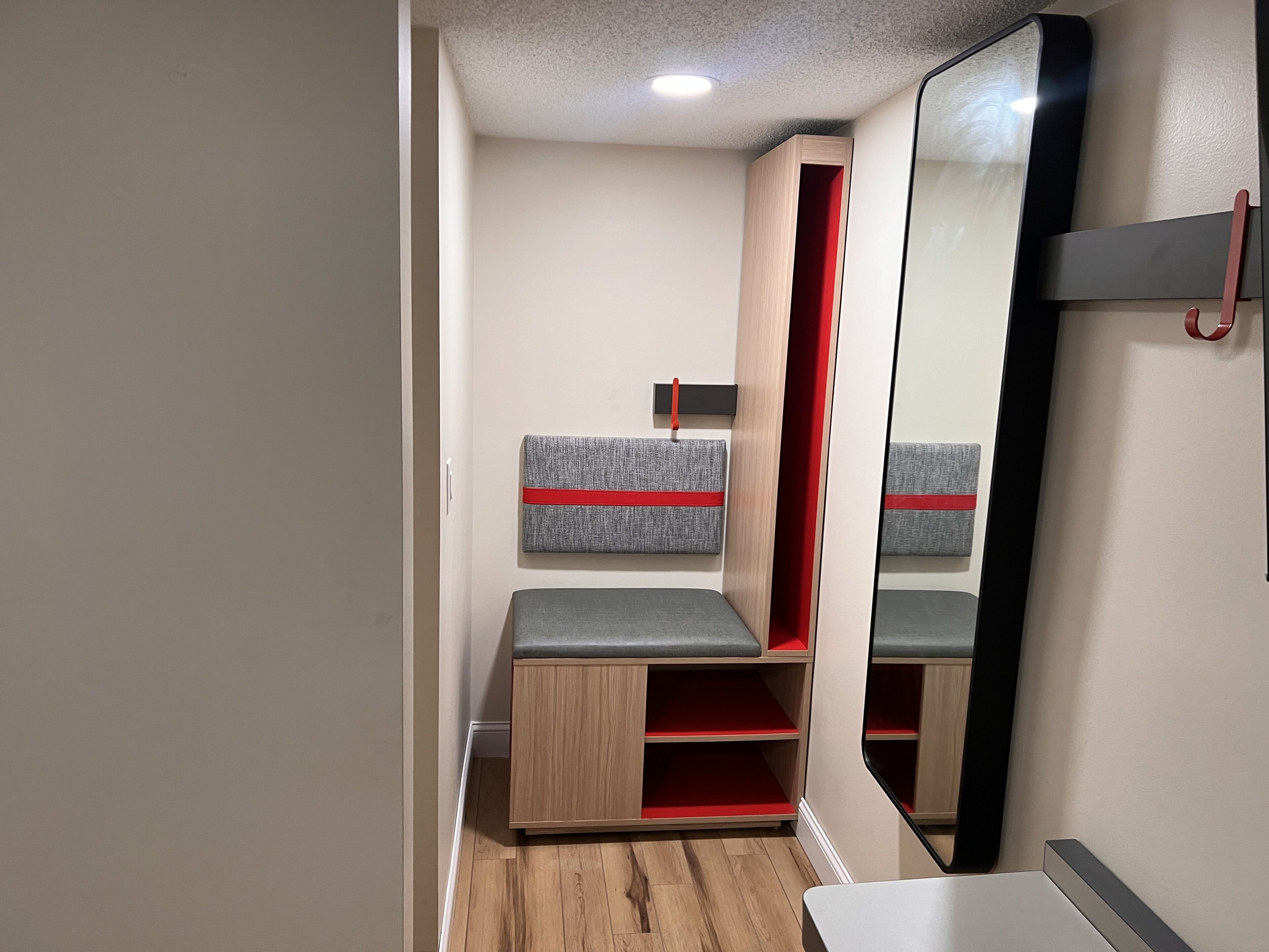 Una habitación compacta con un armario espejo, una banca con detalles rojos y una pequeña mesa.