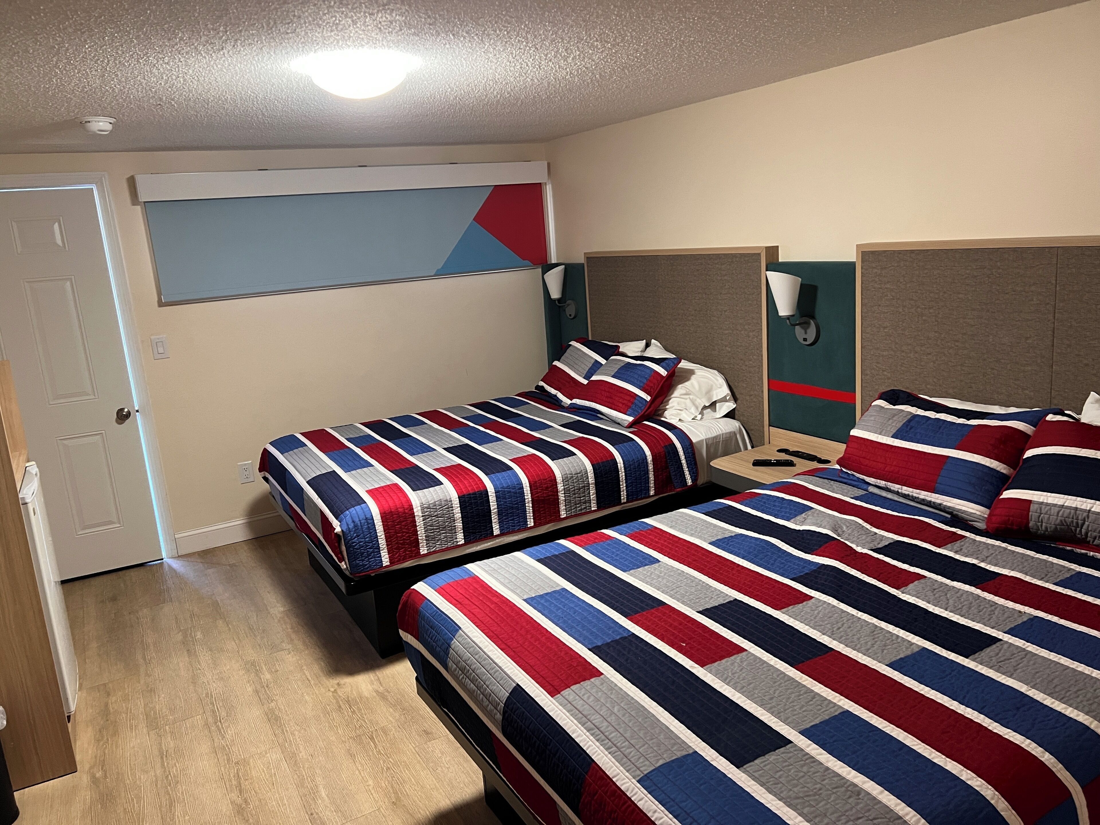 Habitación de hotel con dos camas, cada una con colcha a rayas, una mesita de noche y un televisor montado en la pared.
