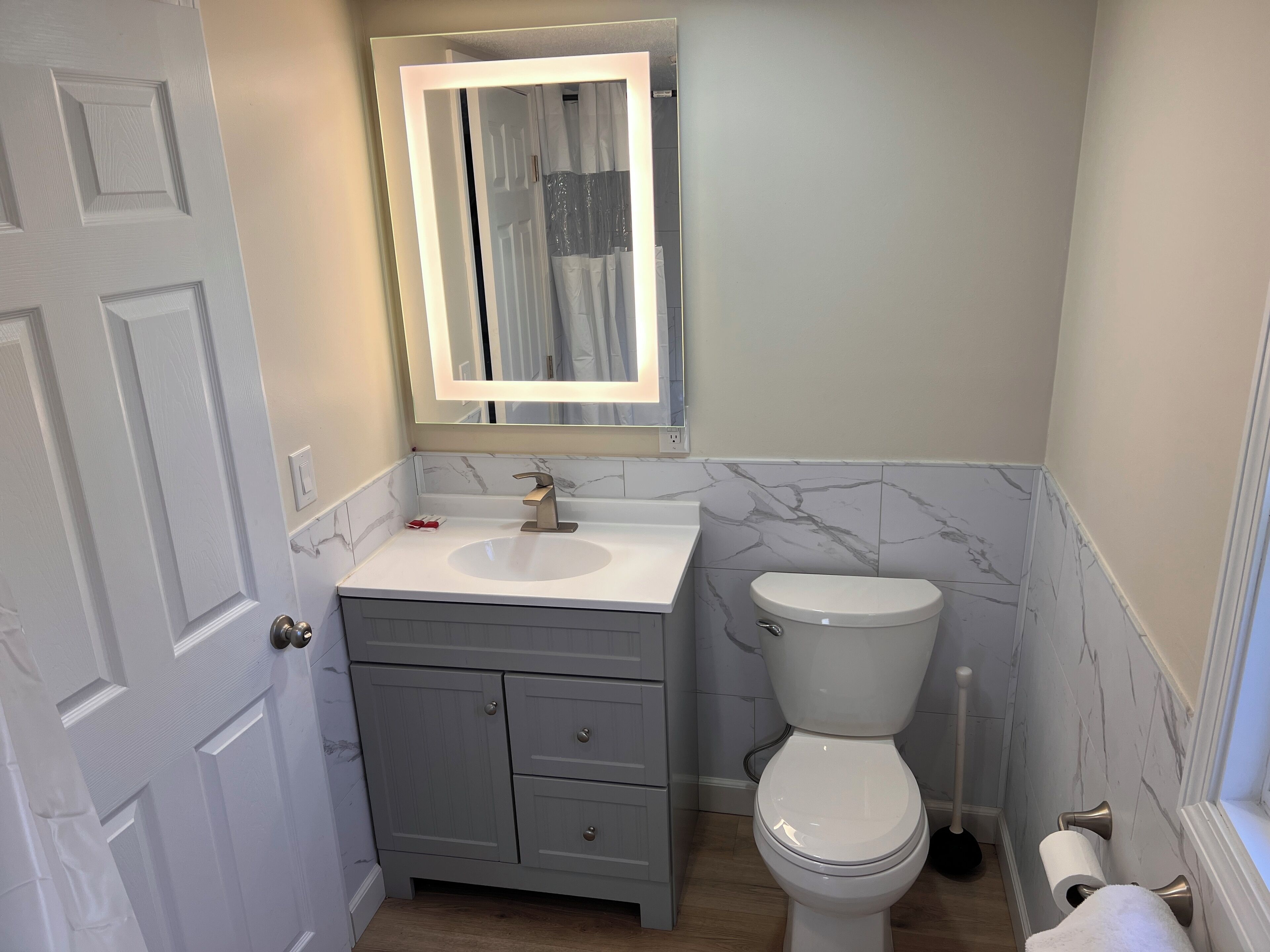 A bathroom with a white sink, a toilet, and a mirror with a light.