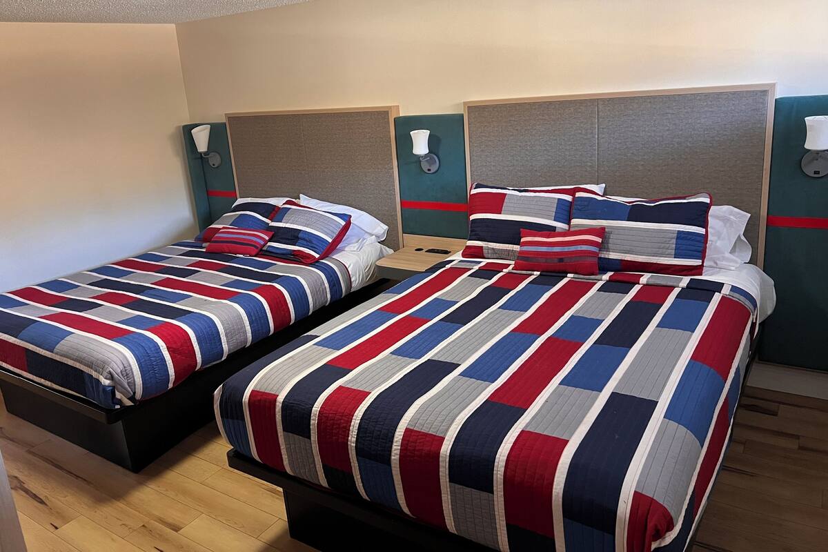A hotel room with two beds, each with a striped bedspread and matching pillows.