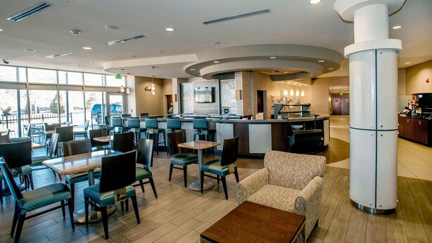 A modern hotel lobby with a central bar area, seating arrangements, and a large pillar. - SpringHill Suites Pueblo Downtown (Pueblo)