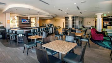 Un moderno hall de hotel con área de bar, asientos y una pantalla de televisión.