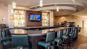 A bar area with a TV screen, multiple liquor bottles, and bar stools. - SpringHill Suites Pueblo Downtown (Pueblo)