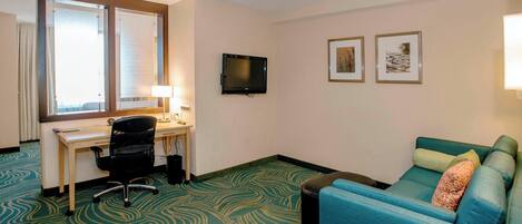 Una habitación de hotel con escritorio, televisión, sofá y alfombra estampada.