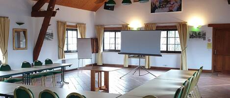 Un salón amplio con techos altos de madera, varias mesas y sillas, y una pizarra grande.