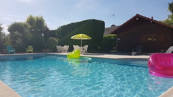 Relax by the inviting pool surrounded by lush hedges and a charming wooden building.