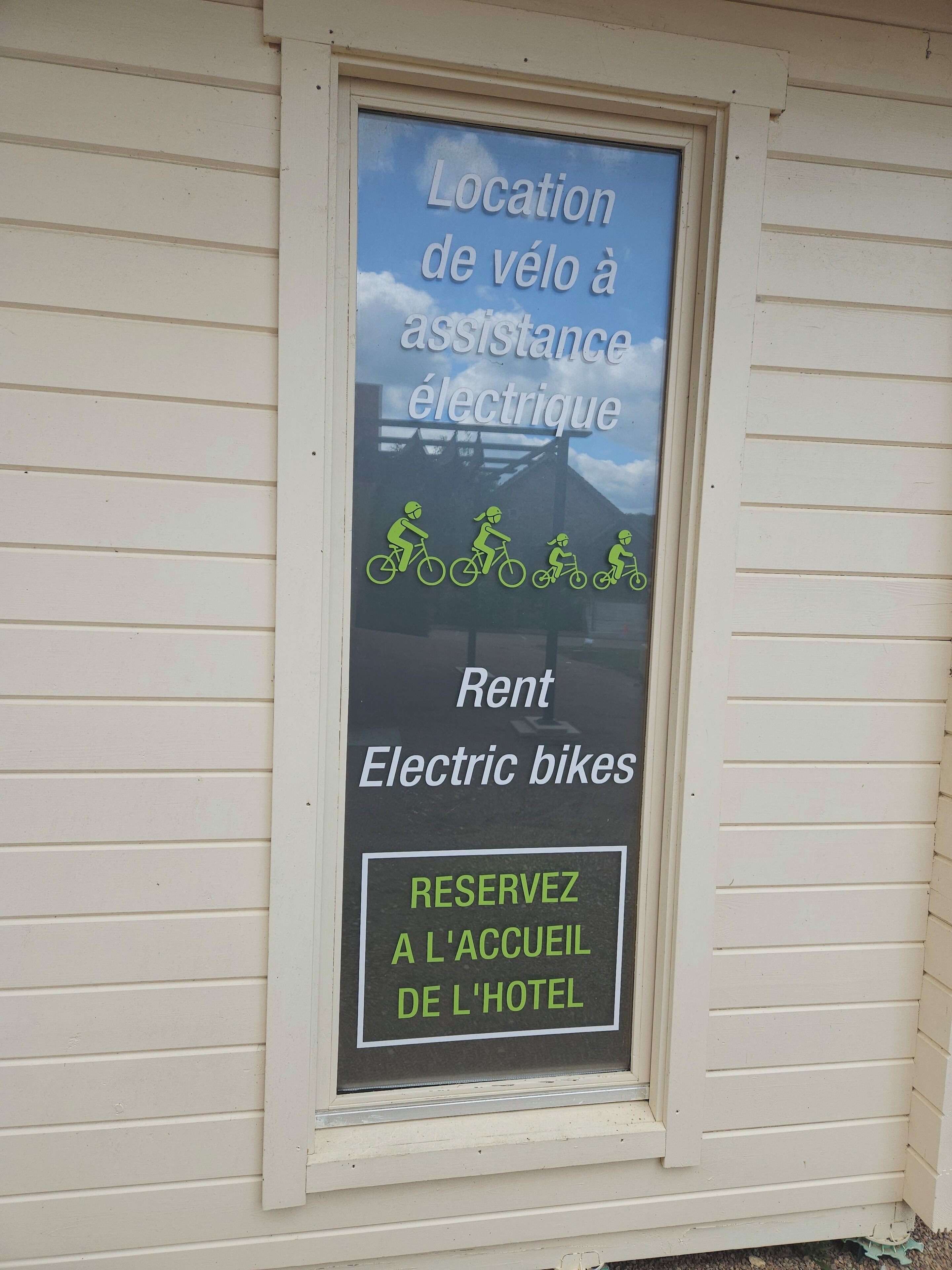 Una ventana con un letrero que indica un lugar para asistencia y alquiler de bicicletas eléctricas.