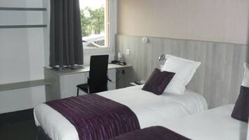 A hotel room with two beds, a desk, a chair, and a window.