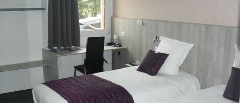A hotel room with two beds, a desk, a chair, and a window.