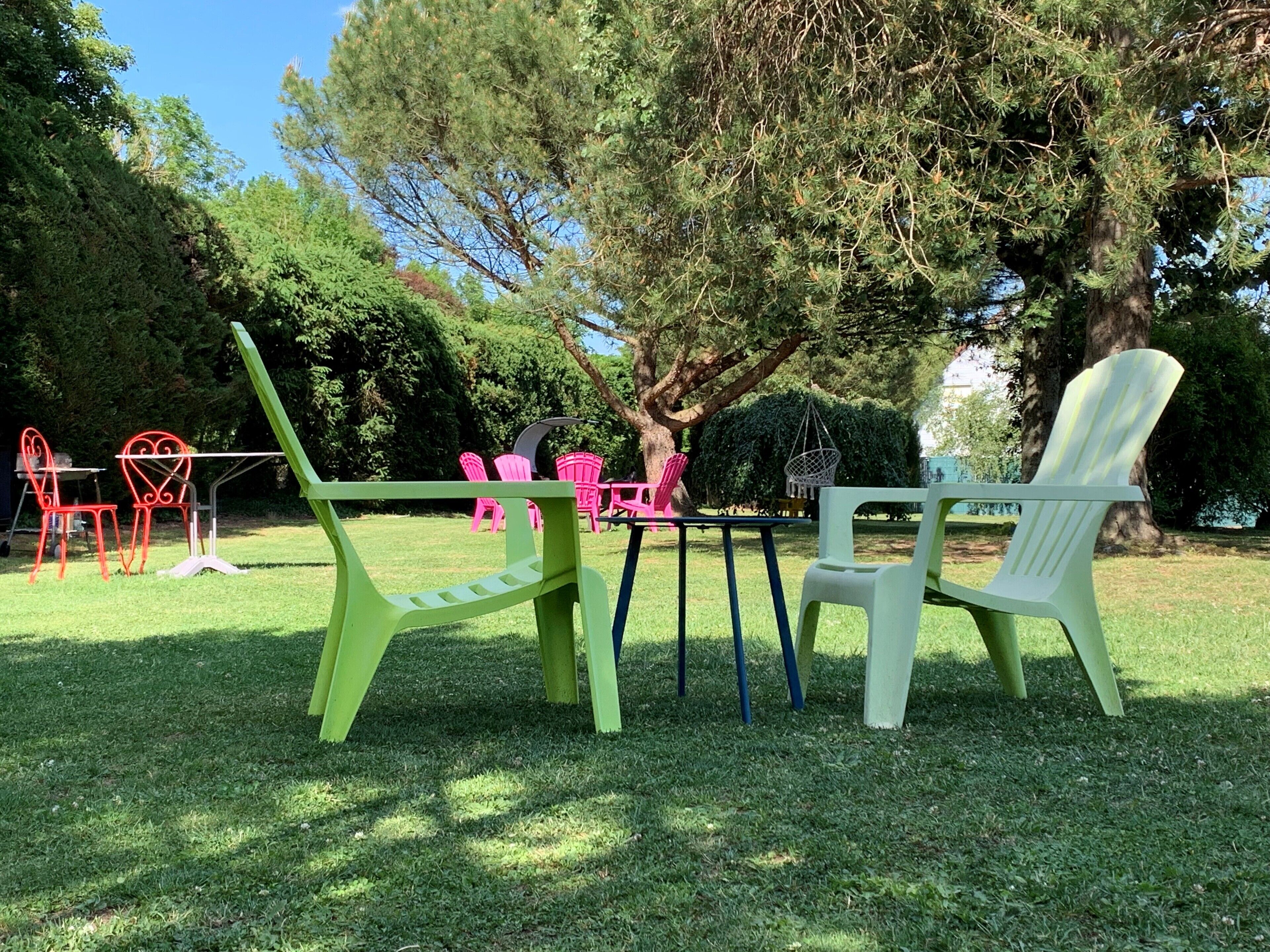 A grassy outdoor area with a table and chairs, surrounded by trees and bushes.