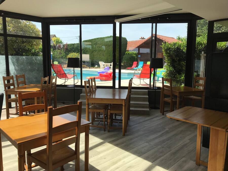 Un patio soleado con mesas y sillas de madera, una piscina y sillones de colores.