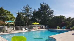 Una piscina con solárium empedrado, rodeada de sillas de descanso y sombrillas.