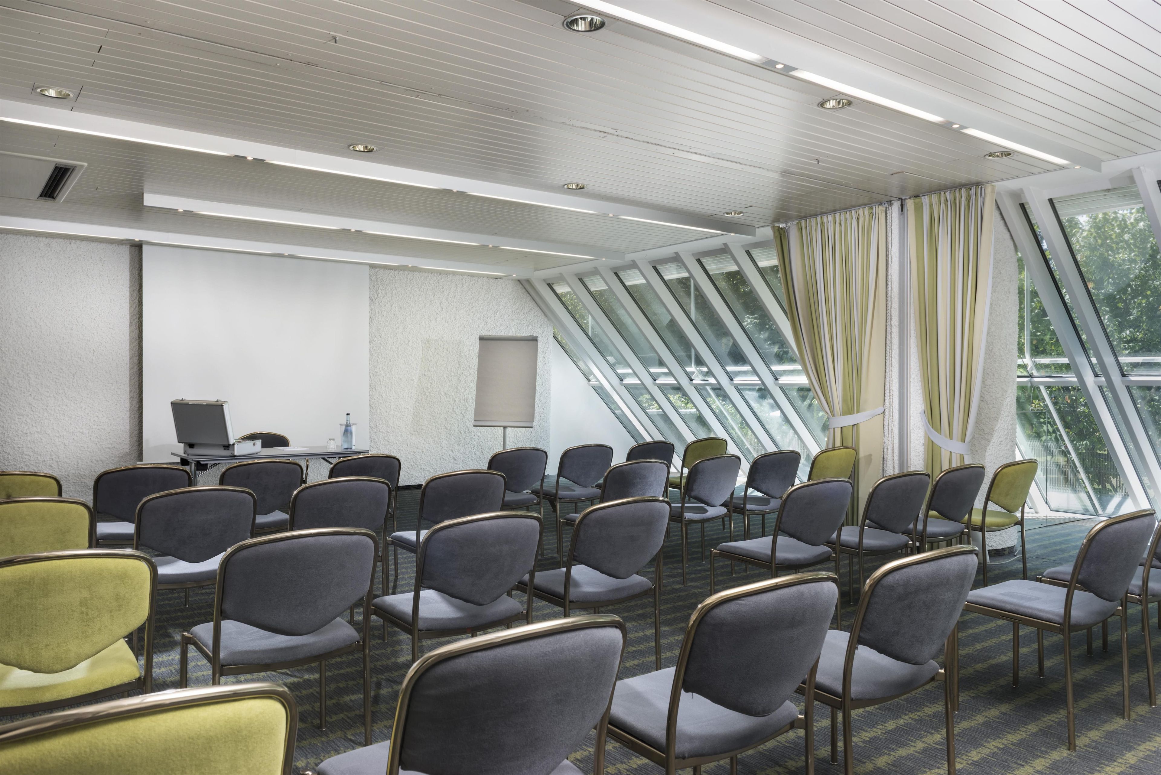 A conference room with rows of chairs, a projector, and a large window with curtains.