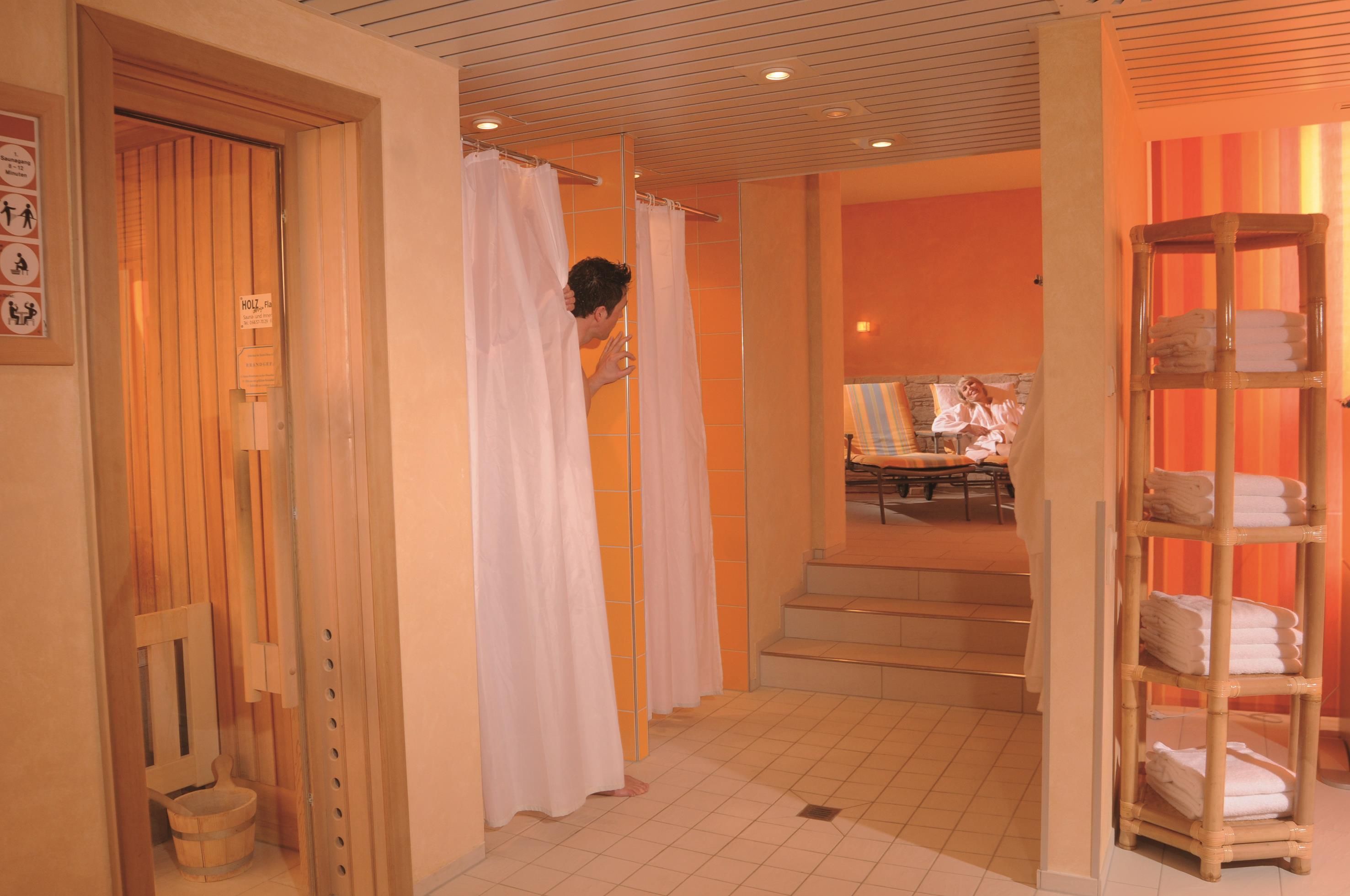 A hotel bathroom with wooden doors, a shower area, and a shelf with towels.