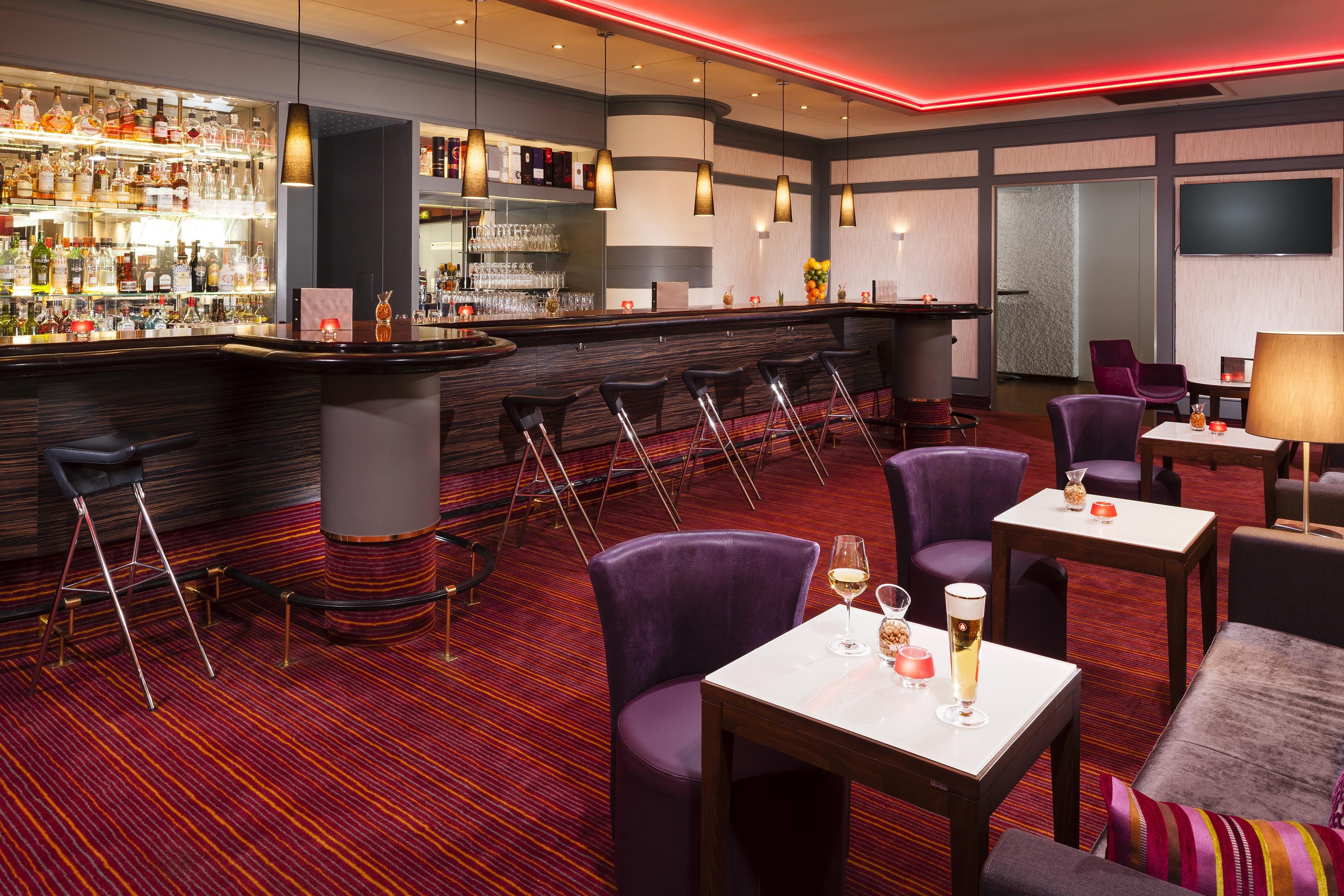 A bar area with stools, a bar counter, and a variety of bottles and glasses.