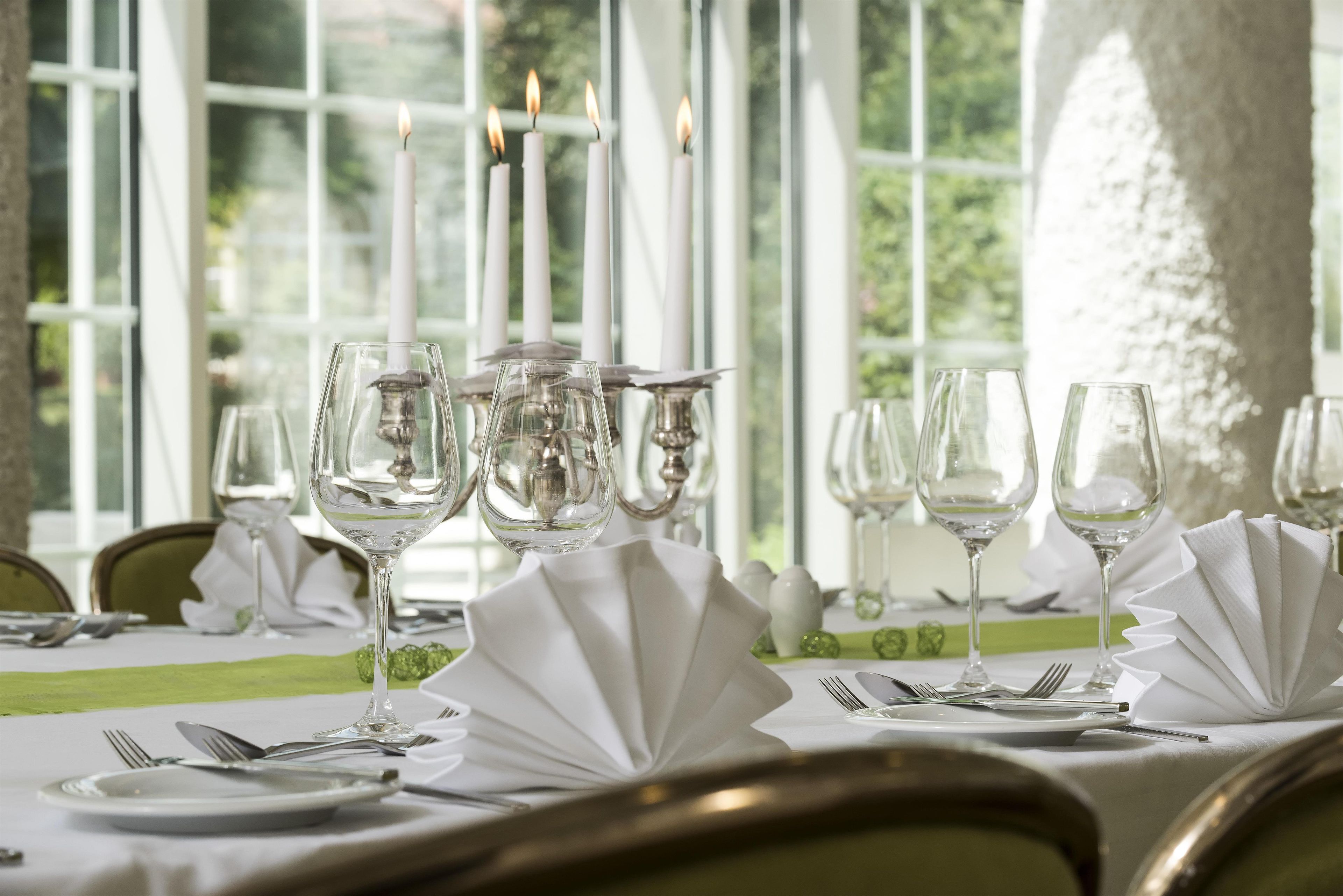 Une table à manger dressée avec des nappes blanches, de la vaisselle en verre transparent et des bougies.