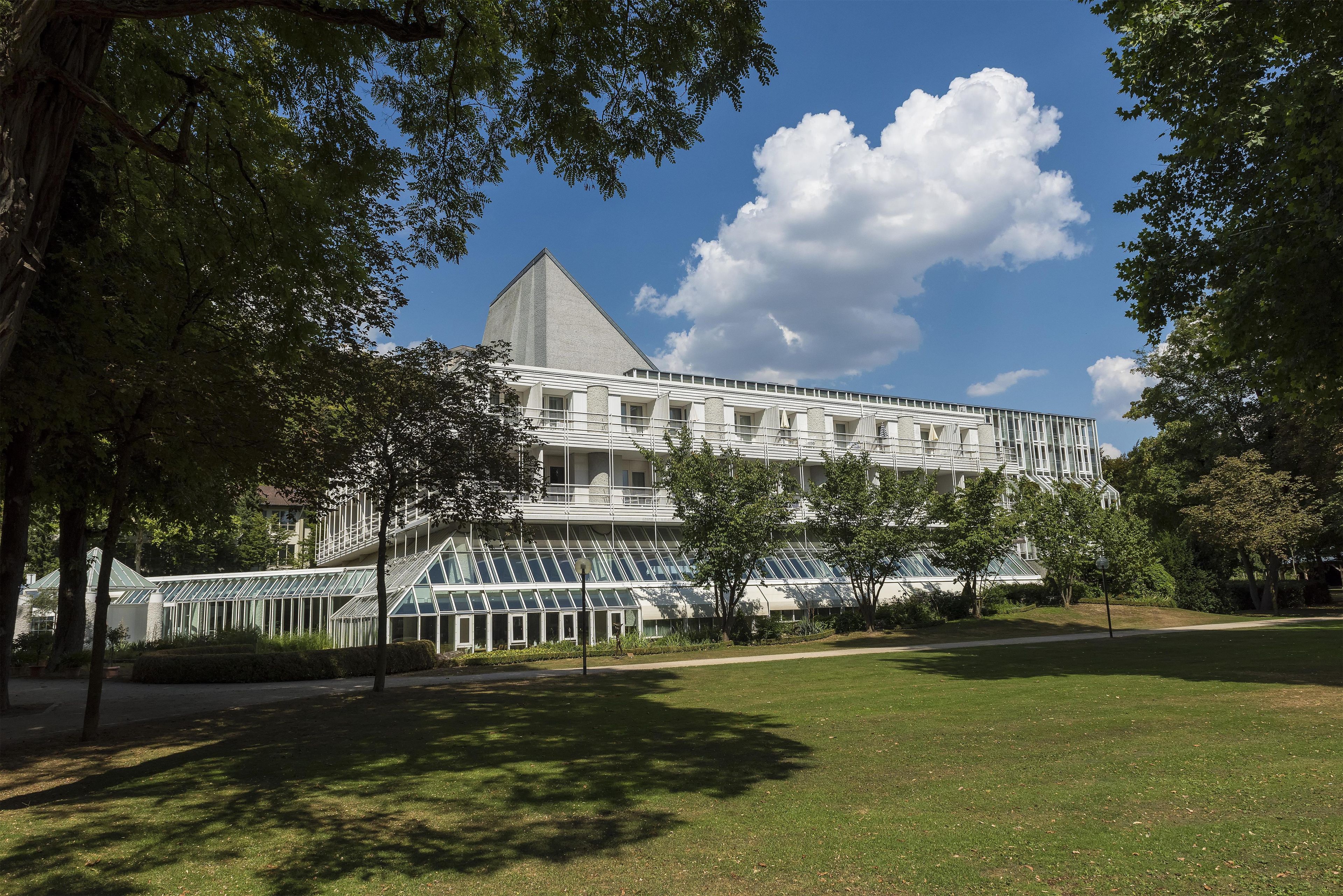 A modern building with a prominent triangular roof, surrounded by a well-maintained lawn and trees.