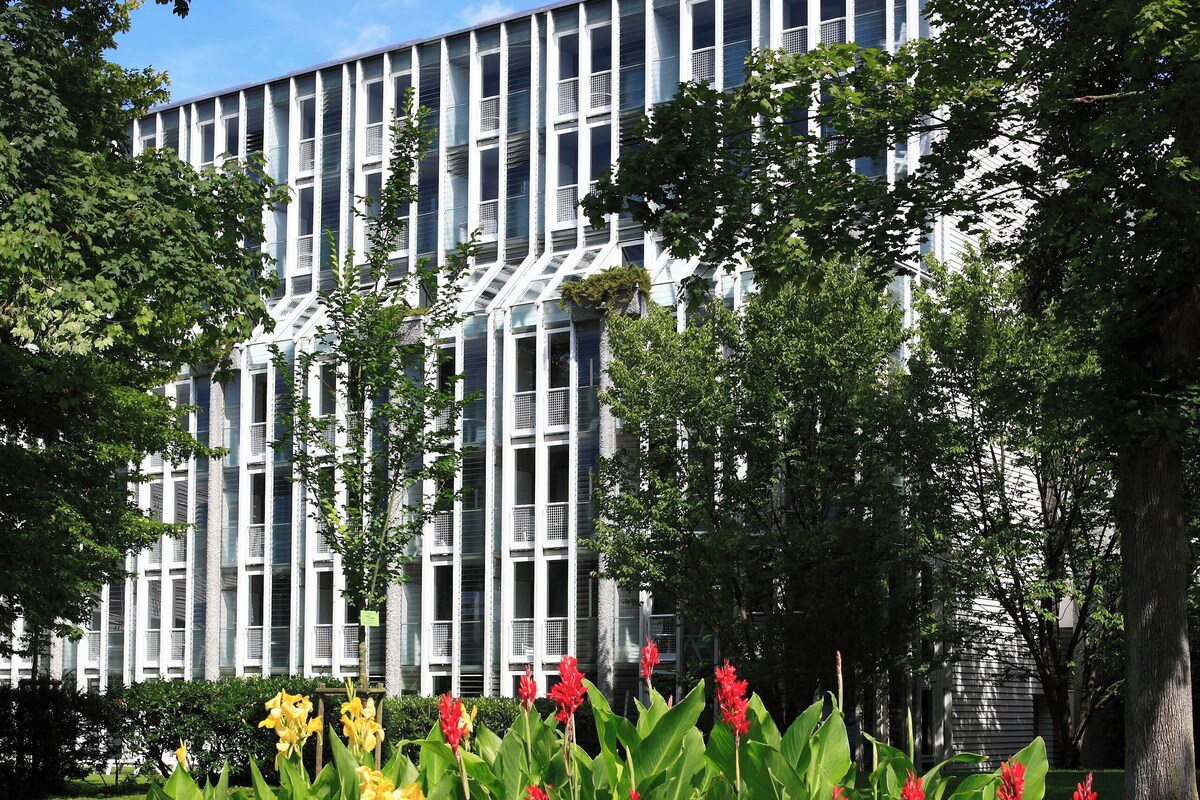 A modern building with a grid-like facade, surrounded by a well-maintained garden with various flowering plants.