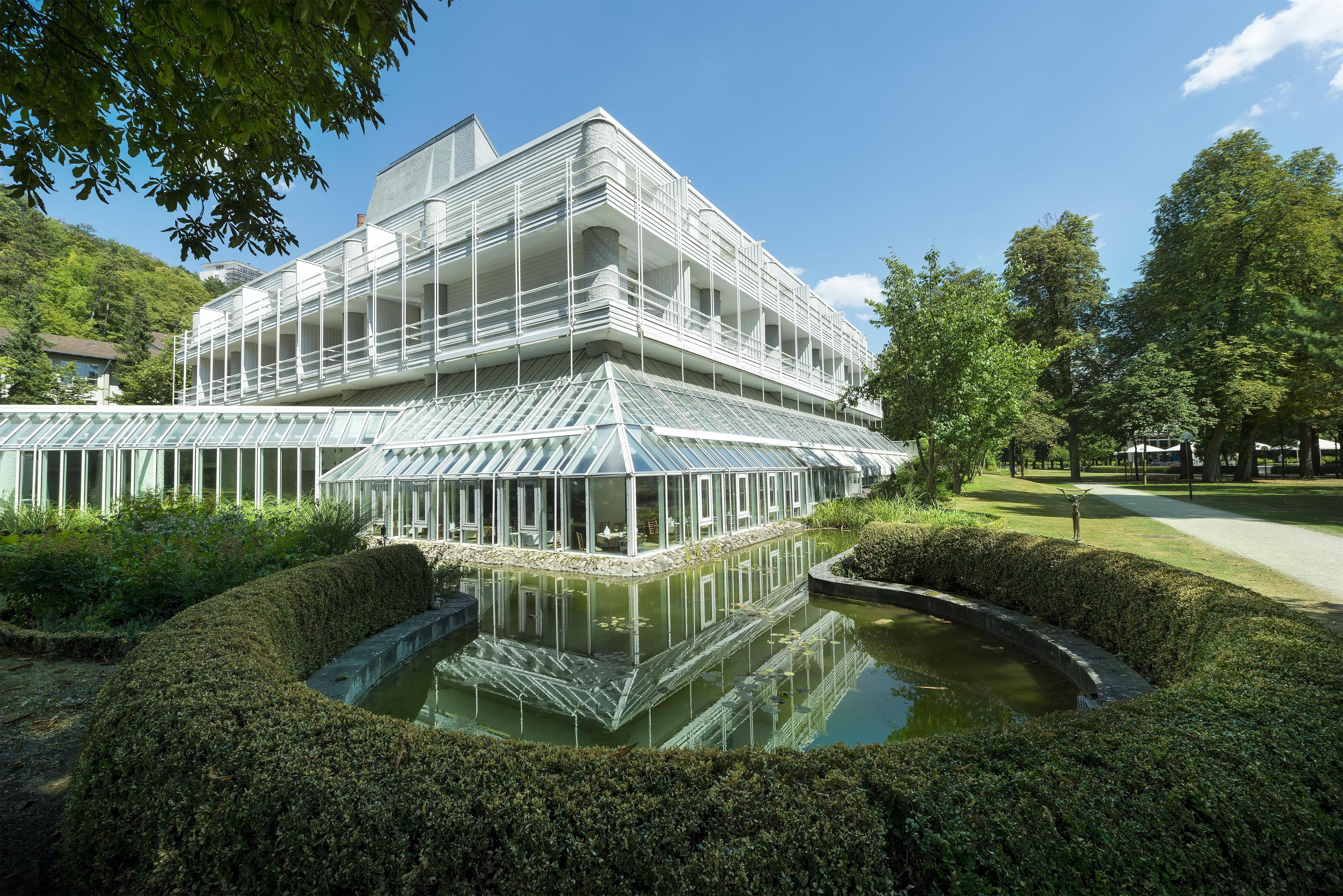 Un edificio moderno con una serra in vetro e un elemento d'acqua riflettente.