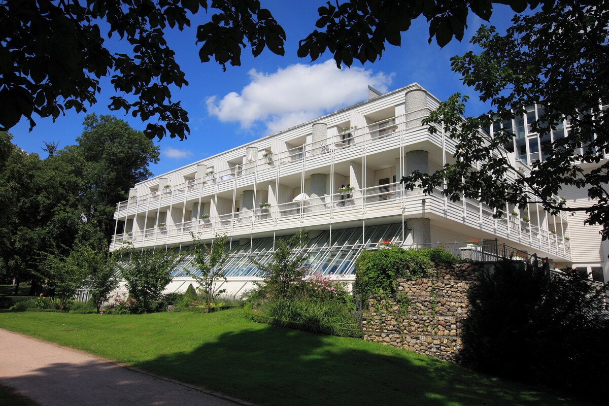 A multi-story hotel with balconies, a stone wall, and lush greenery.