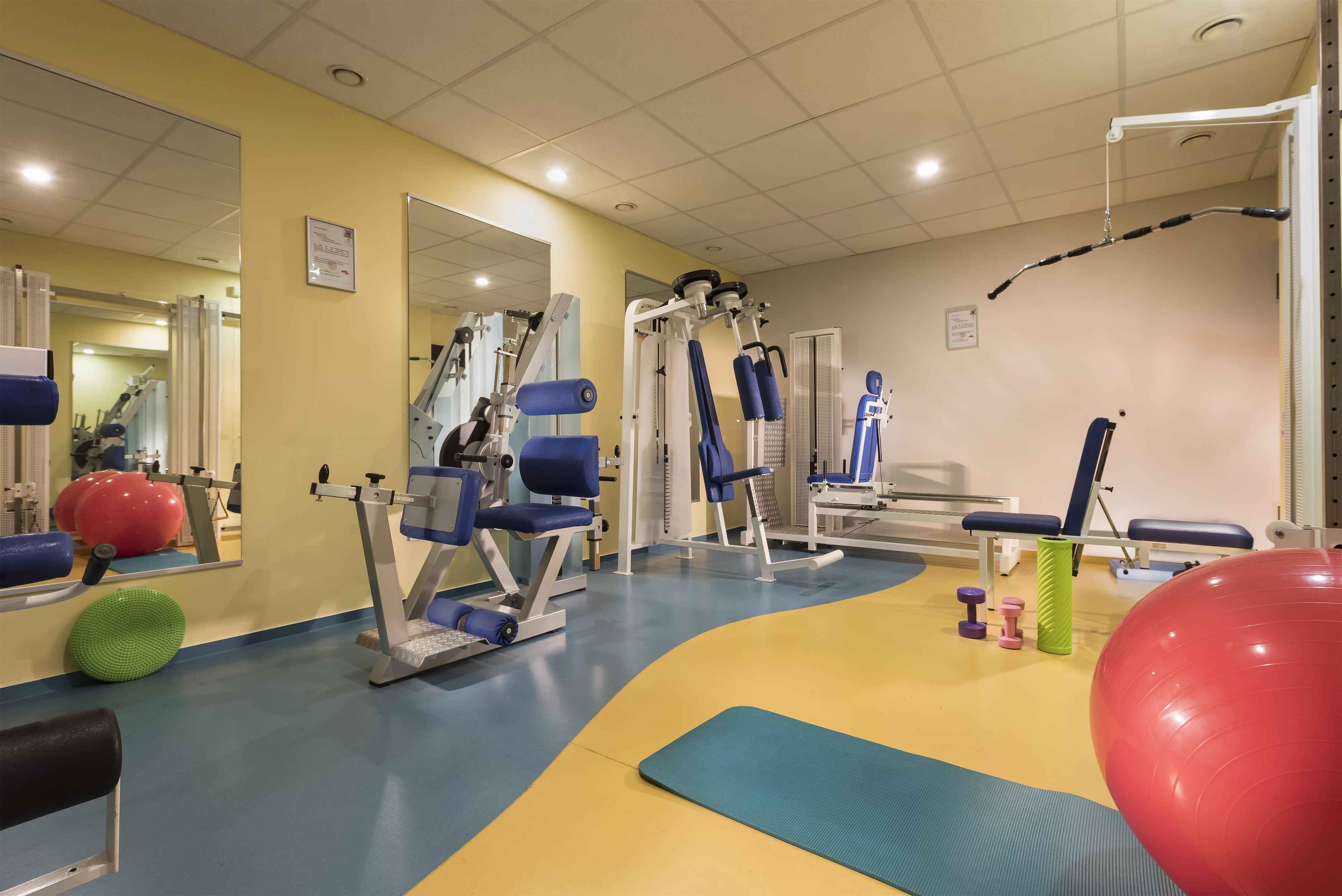 Ein Fitnessraum mit Trainingsgeräten, einem Spiegel und Übungsbällen.