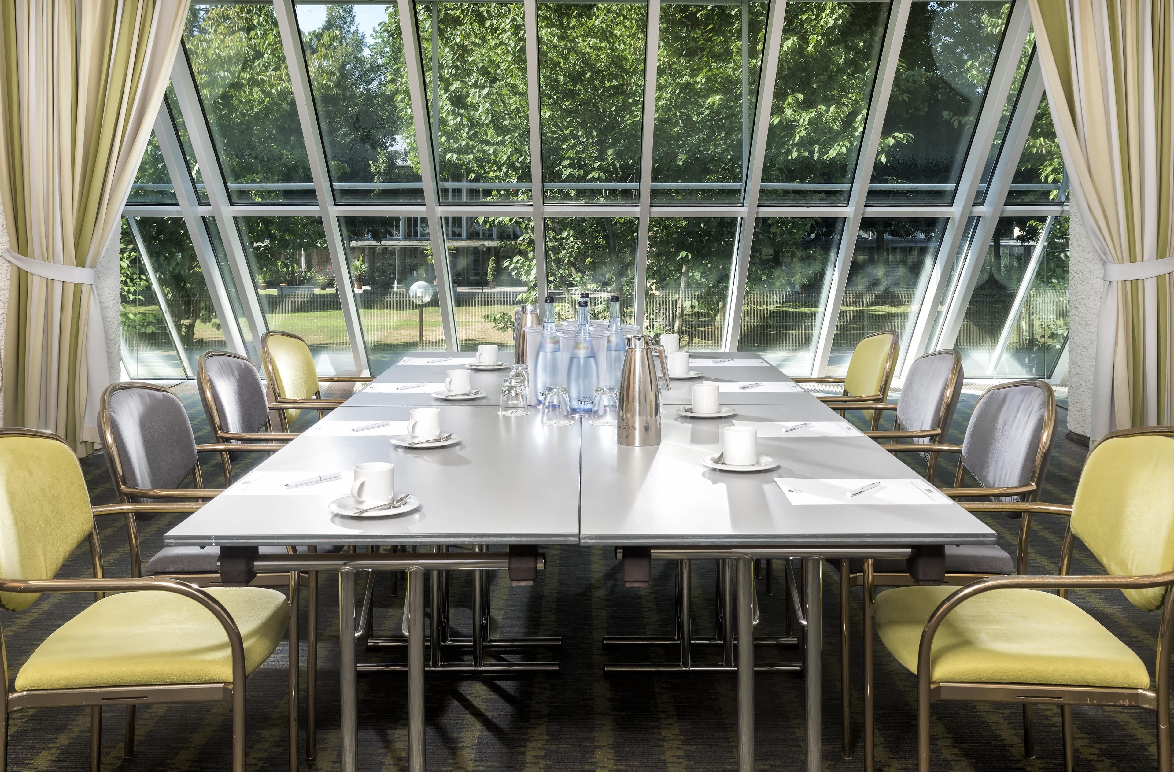 Ein Konferenzraum mit einem langen Tisch, Stühlen und Blick auf Grün hinter großen Fenstern.