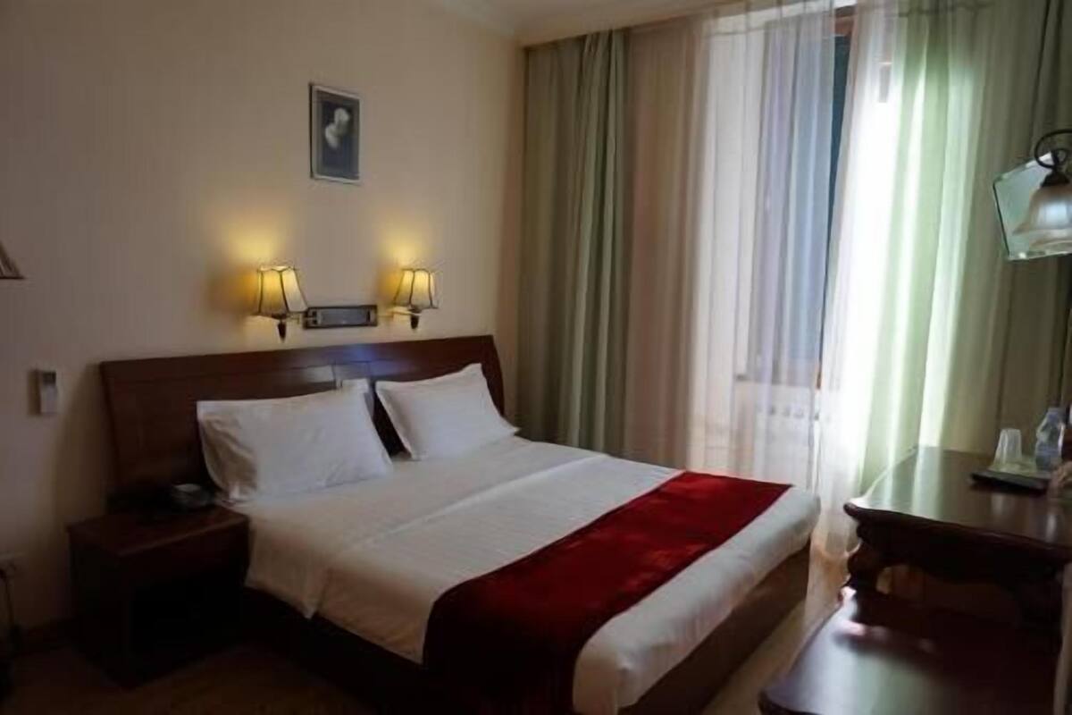 Hotellihuone, jossa on sänky, yöpöydät, työpöytä ja lamppu.