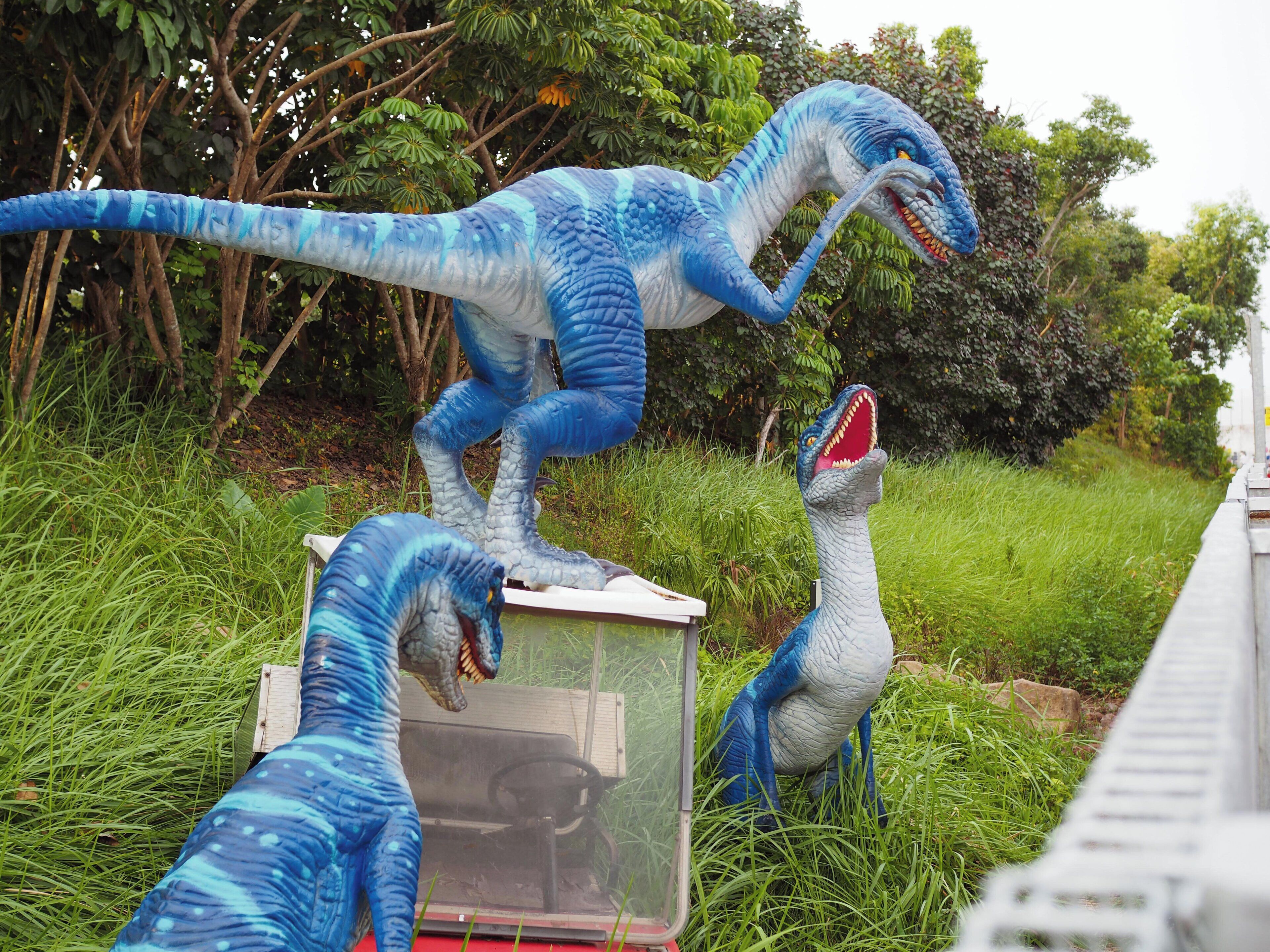 A dinosaur exhibit with a large blue dinosaur model standing on a platform, surrounded by greenery.